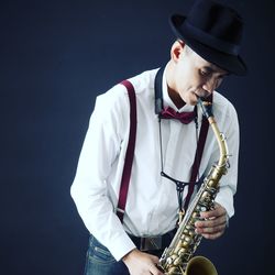 Musician playing saxophone while standing against black background