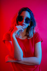 Beautiful young woman wearing sunglasses against red background