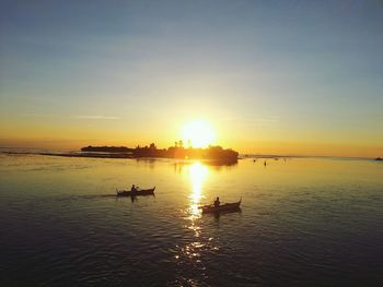 Silhouette people on sea against sky during sunset