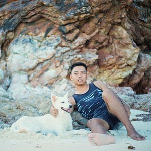 Portrait of young woman with dog sitting on rock