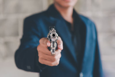 Midsection of man holding gun while standing against wall