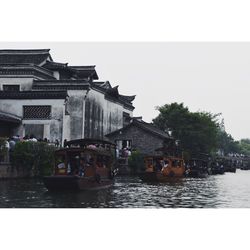 Boats in river by buildings against clear sky