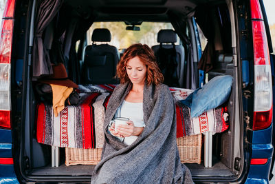 Woman holding mug while sitting in camper trailer