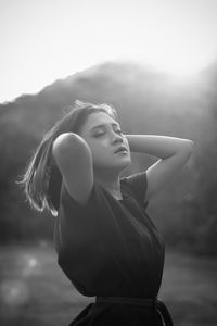 Woman with hand in hair standing against sky