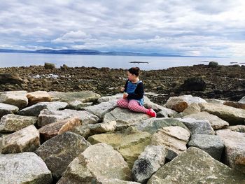 Girl sitting on rock by sea against sky