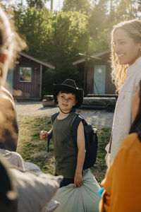 Boy wearing hat and backpack standing with friends at summer camp