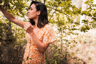 Young woman looking away while standing against tree