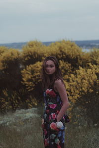 Portrait of young woman standing on field against sky