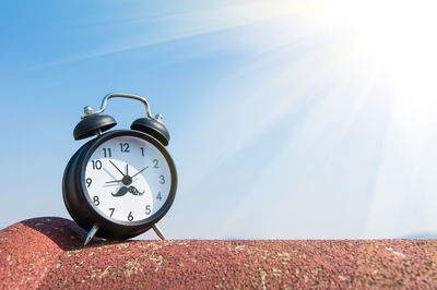 Low angle view of alarm clock against blue sky