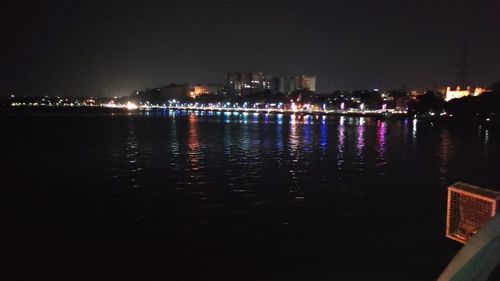 Illuminated buildings by river against clear sky at night