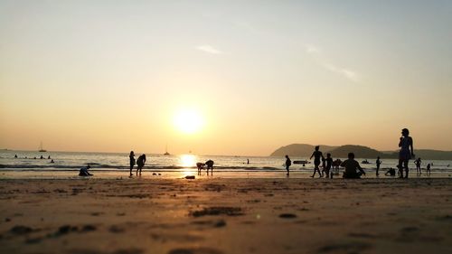 Silhouette of people on beach against sky during sunset