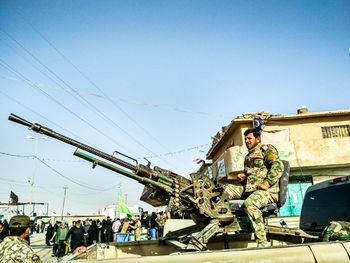 Army soldier sitting by cannon against clear sky