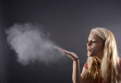 Woman blowing powder paint against gray background