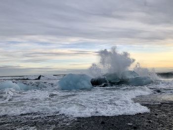 Sea waves splashing on rocks against sky