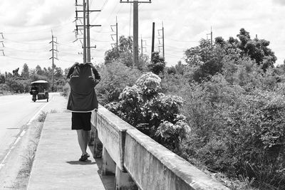 Rear view of man walking on sidewalk by trees against sky