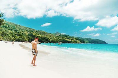 Shirtless man walking at beach against sky