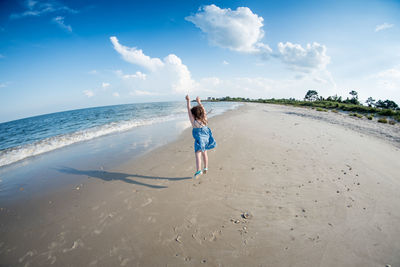 Rear view of girl jumping on beach against sky