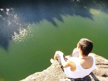 Rear view of shirtless man sitting by lake