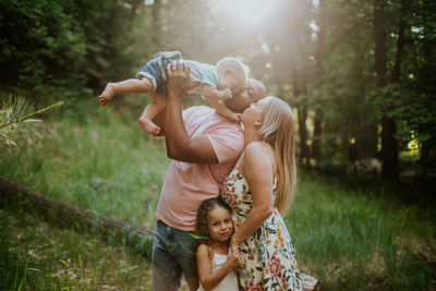 Family of four snuggling and kissing in forest