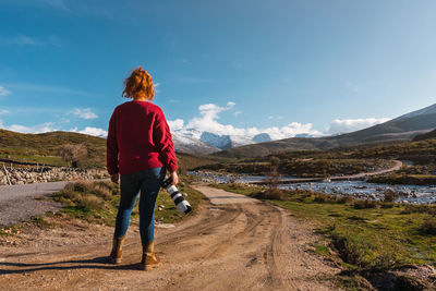 Unrecognizable woman standing on the road by the river with a camera with snowy mountains