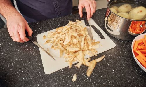 Midsection of man with knives by potato peels on cutting board