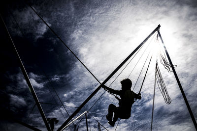 Low angle view of silhouette man hanging on rope against sky