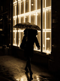 Full length of man standing on wet street at night