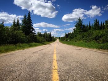 Empty road amidst trees against sky