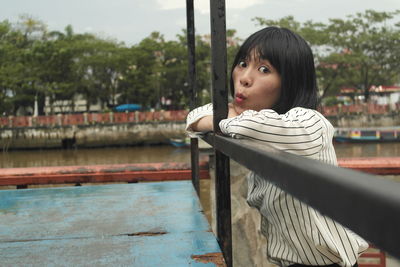 Portrait of young woman looking away against railing