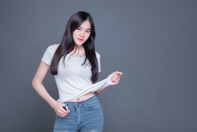 Portrait of young woman standing against gray background