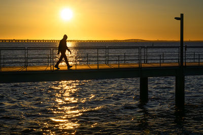Silhouette man walking on pier against sky during sunset