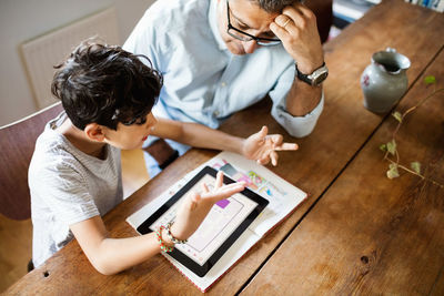 High angle view of father and son discussing over digital tablet while studying at home