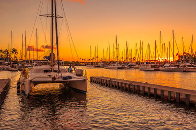 Sailboats moored on sea against sky during sunset