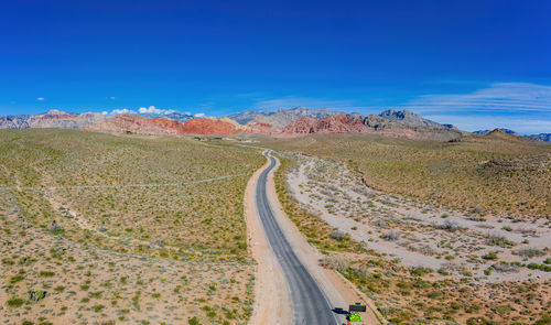 Panoramic view of road amidst desert against blue sky