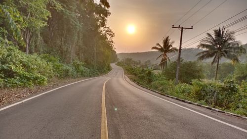 Empty road amidst trees against sky during sunset