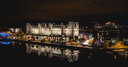 Illuminated buildings by river against sky at night