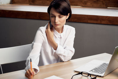 Mid adult woman using mobile phone while sitting on table