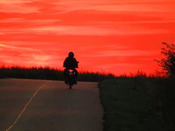 Rear view of silhouette man riding motorcycle against orange sky