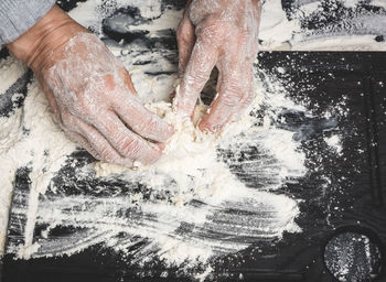 Two female hands knead the dough from white wheat flour on a black table, top view