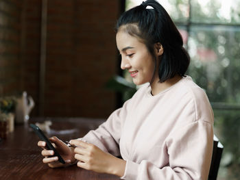 Young woman using smart phone on table at window