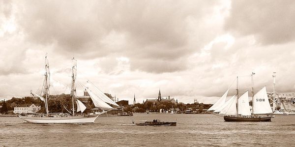 Boats moored at harbor against cloudy sky