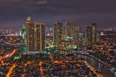 Illuminated modern buildings in city against sky at night