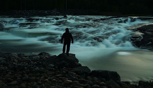 Silhouette man standing at riverbank during night