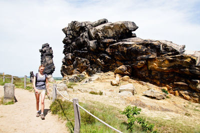 Woman standing on rock formation against sky