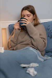 Sick woman drinking coffee resting on bed