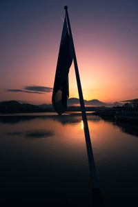 Silhouette pole by lake against sky during sunset