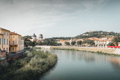 Houses by river and buildings in town against sky