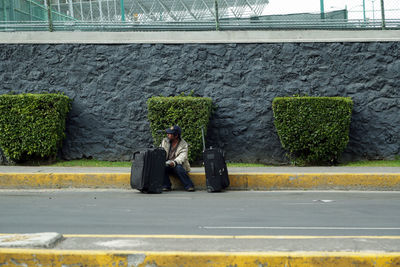 Man sitting on footpath against wall