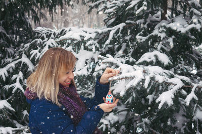 Smiling woman with christmas ornament in snow during winter