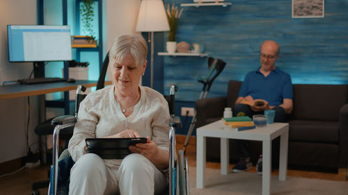 Senior woman using digital tablet while sitting on chair at home